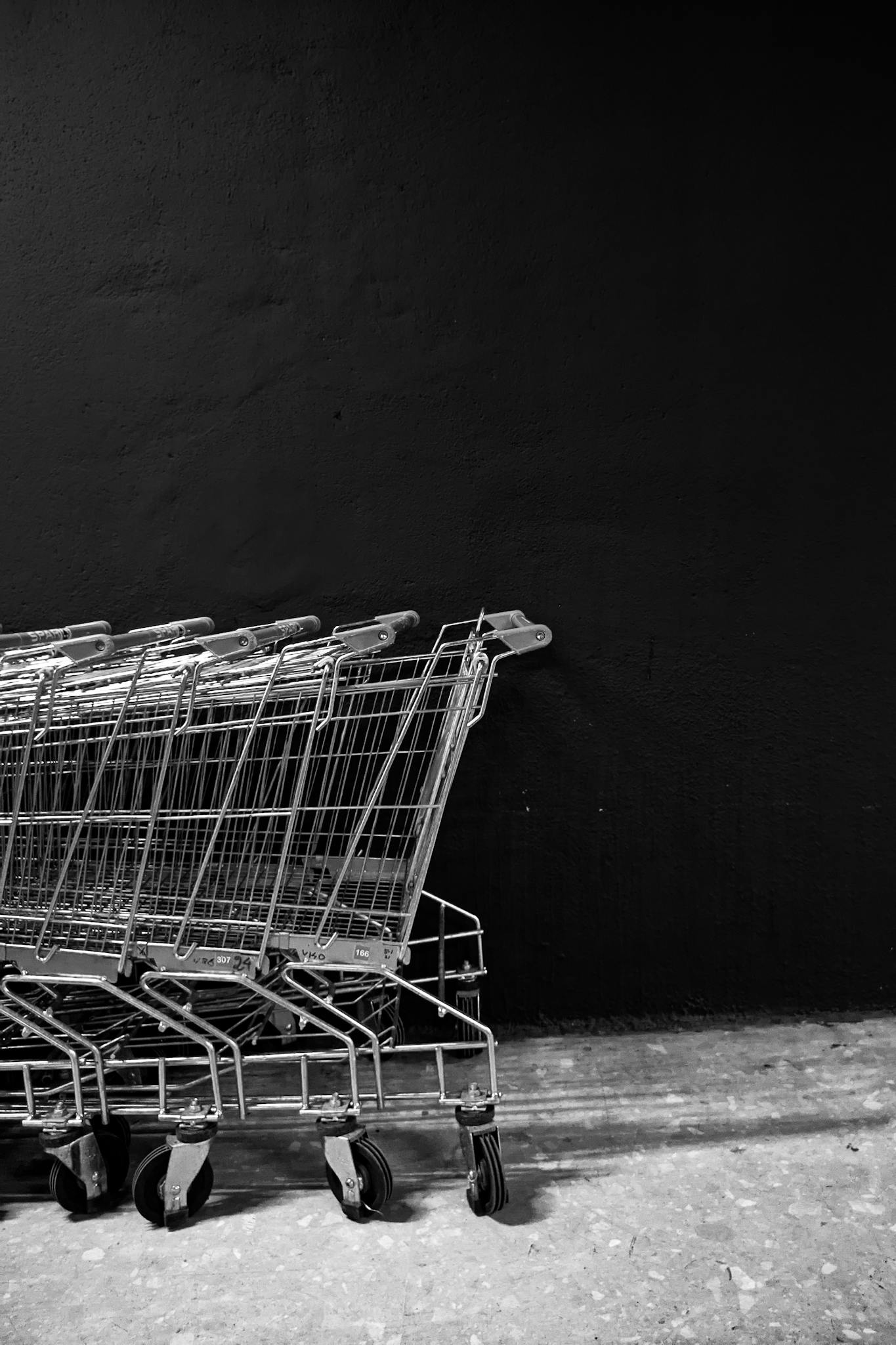 Black and white white of empty shopping trolleys standing on asphalt near black wall of supermarket